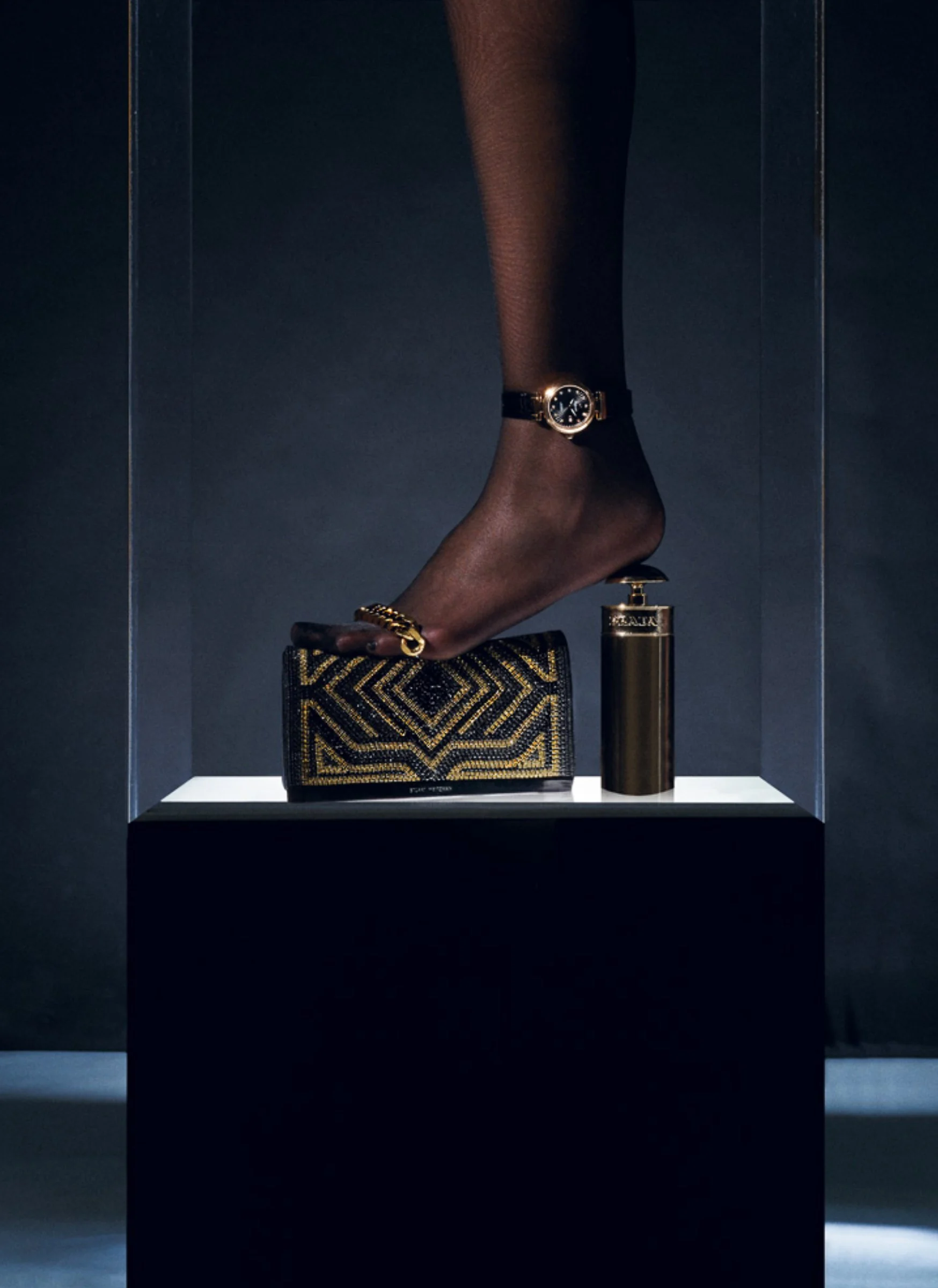 Interview, 2016: a foot in heeled sandals on a gold clutch in a lit display case